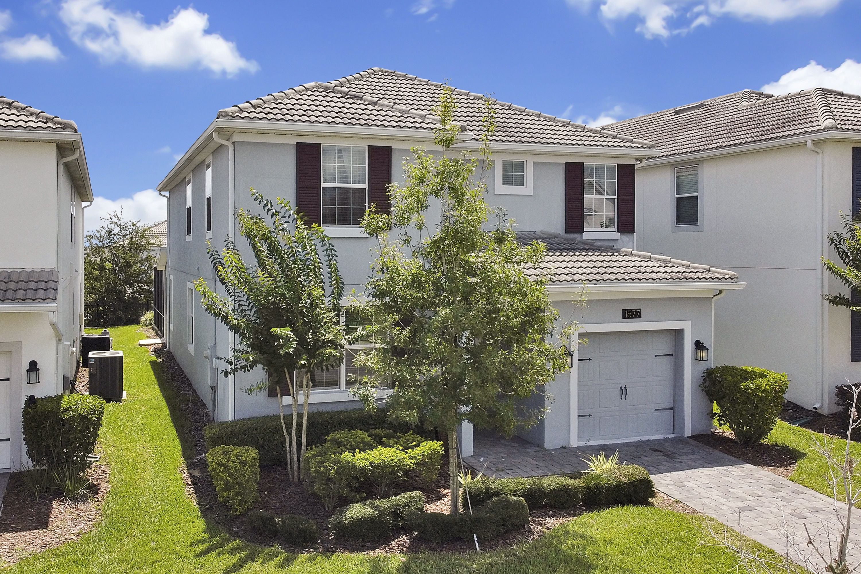 A two-story residential building with a tiled roof, a front garage, and a well-maintained lawn with a small tree.