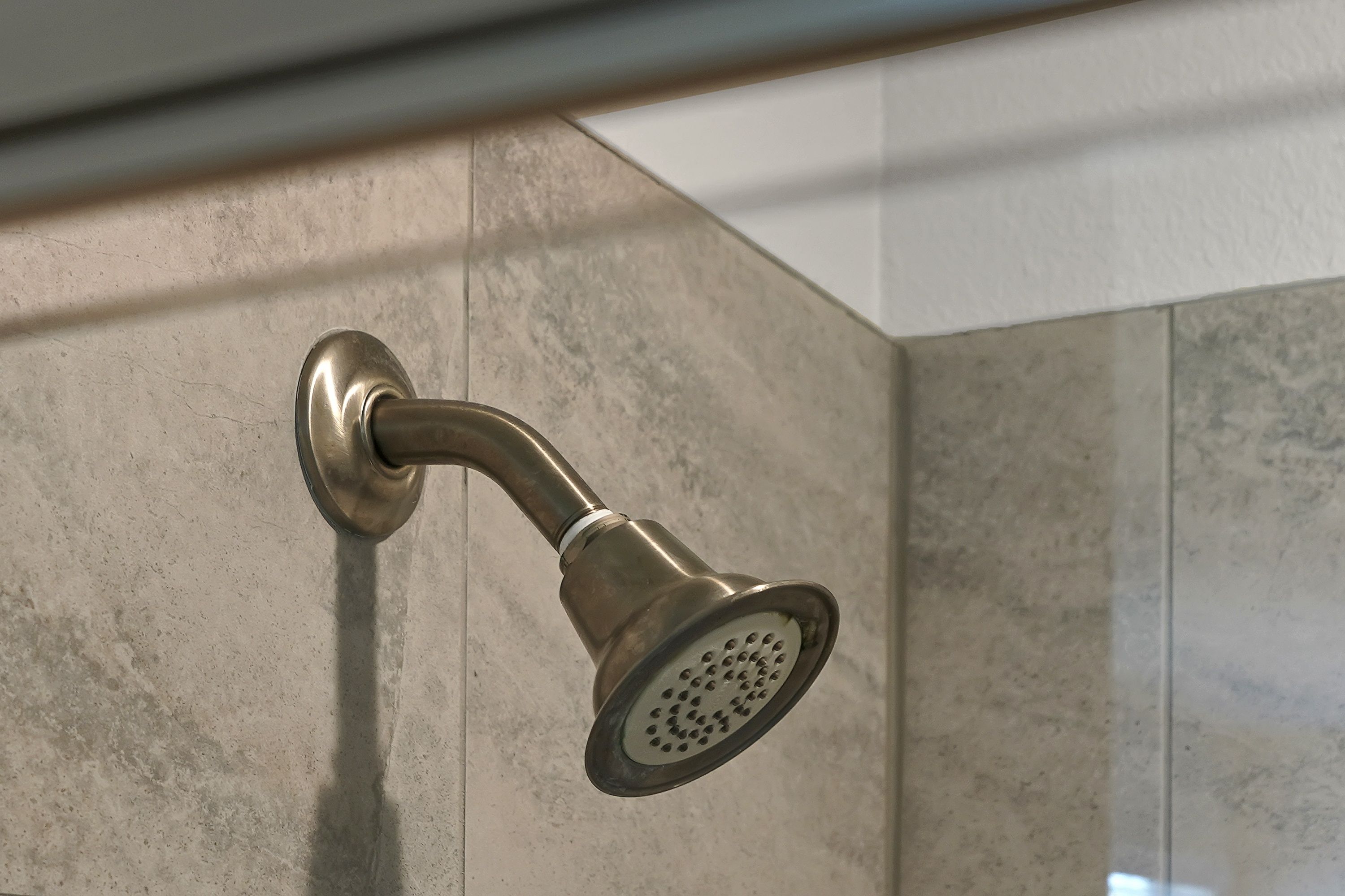 Un pommeau de douche au design incurvé, fixé sur un mur à surface texturée.
