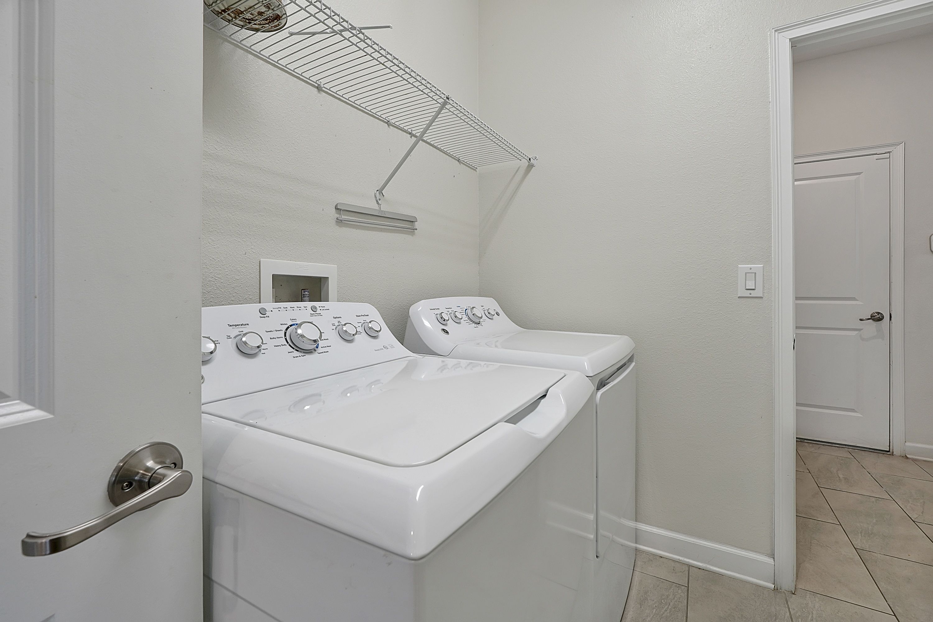 A laundry room with two white front-loading washers and dryers, a metal drying rack, and a white door.