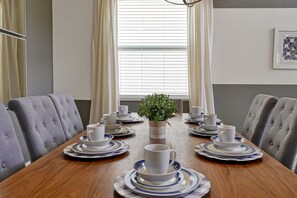 A dining table set with white cups and saucers, a potted plant, and a framed picture on the wall.