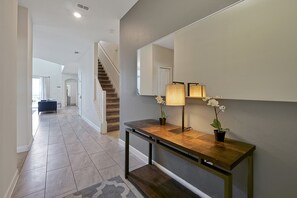 A modern hallway with a wooden console table, a mirror, and two potted orchids. - 5 Bed In Champions Gate, Modern Decor, Kid Themed Rooms, Game Room, Gated Resort! 5 Bedroom Home by RedAwning (Davenport)