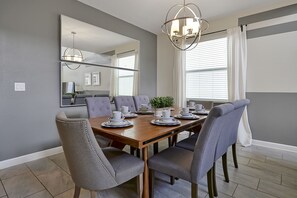 Uma sala de jantar com mesa de madeira posta para seis pessoas, rodeada por cadeiras estofadas cinzentas.