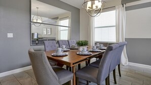 A dining room with a wooden table set for six, grey upholstered chairs, a large mirror, and a modern chandelier. - 5 Bed In Champions Gate, Modern Decor, Kid Themed Rooms, Game Room, Gated Resort! 5 Bedroom Home by RedAwning (Davenport)