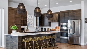 Cocina moderna con armarios de madera oscura, electrodomésticos de acero inoxidable y una isla central con taburetes de bar.