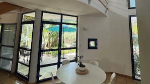 A spacious room with a high ceiling, a spiral staircase, and large windows offering views of the outdoors. - Gîte la Majorelle T3 de 92 m² + Terrasses, Jardin (Saint-Guiraud)