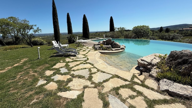 A pool area with lounge chairs, a stone pathway, and tall trees in the background. - Gîte la Majorelle T3 de 92 m² + Terrasses, Jardin (Saint-Guiraud)