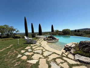 A pool area with lounge chairs, a stone pathway, and tall trees in the background. - Gîte la Majorelle T3 de 92 m² + Terrasses, Jardin (Saint-Guiraud)