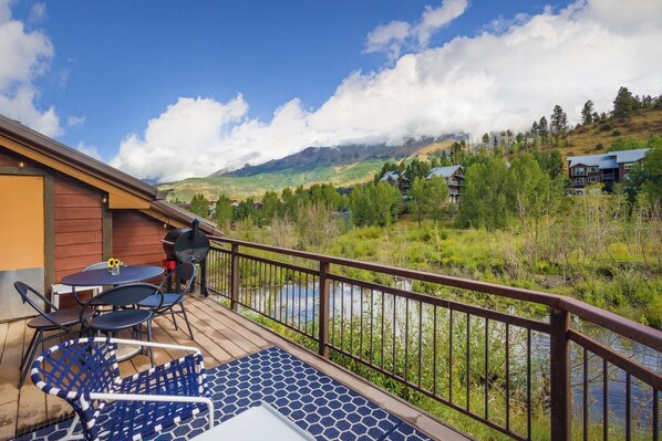 Een houten terras met buitenmeubilair, uitzicht op een rivier en omliggend groen.