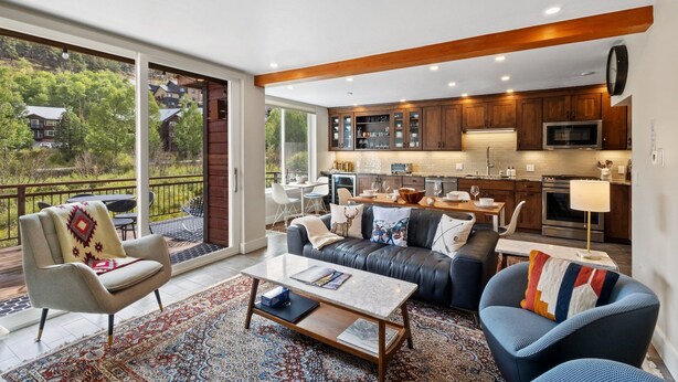 Een moderne woonkamer met een bank, fauteuils en een salontafel. Een groot raam biedt uitzicht op de omgeving.