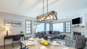 A modern living room with a dining area, large windows, a fireplace, and a mounted TV. - Etta Place 111 2 Bedroom Condo by RedAwning (Telluride)