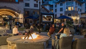 An outdoor seating area with wicker furniture and a central fire pit, surrounded by buildings with balconies and outdoor seating. - Etta Place 111 2 Bedroom Condo by RedAwning (Telluride)