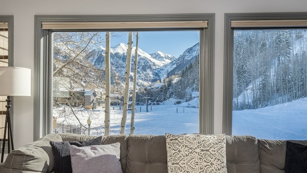 A living room with a large window offering a view of snow-covered mountains and a village. - Etta Place 111 2 Bedroom Condo by RedAwning (Telluride)