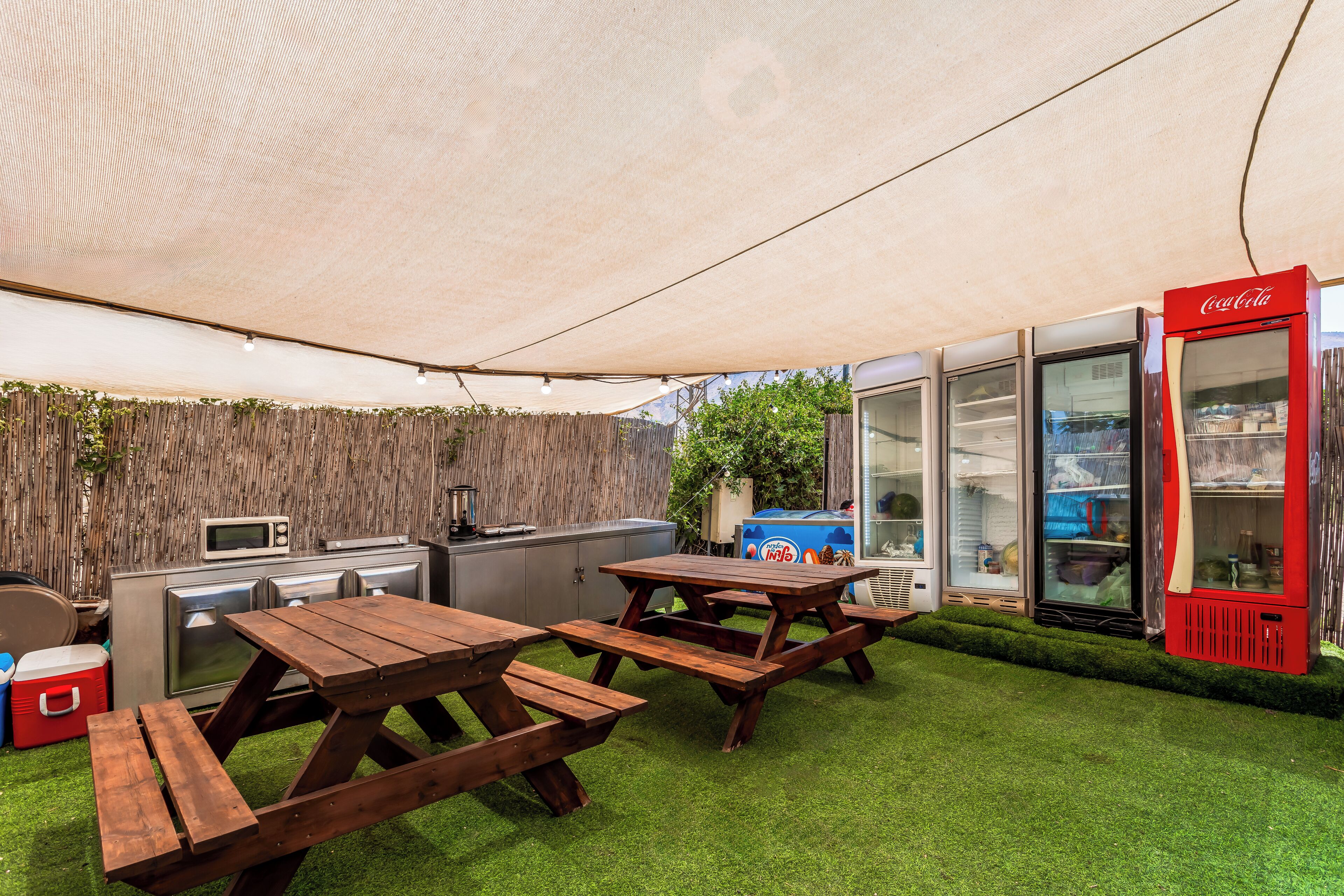 Een terras buiten met picknicktafels, een barbecue en een Coca-Cola koelkast.