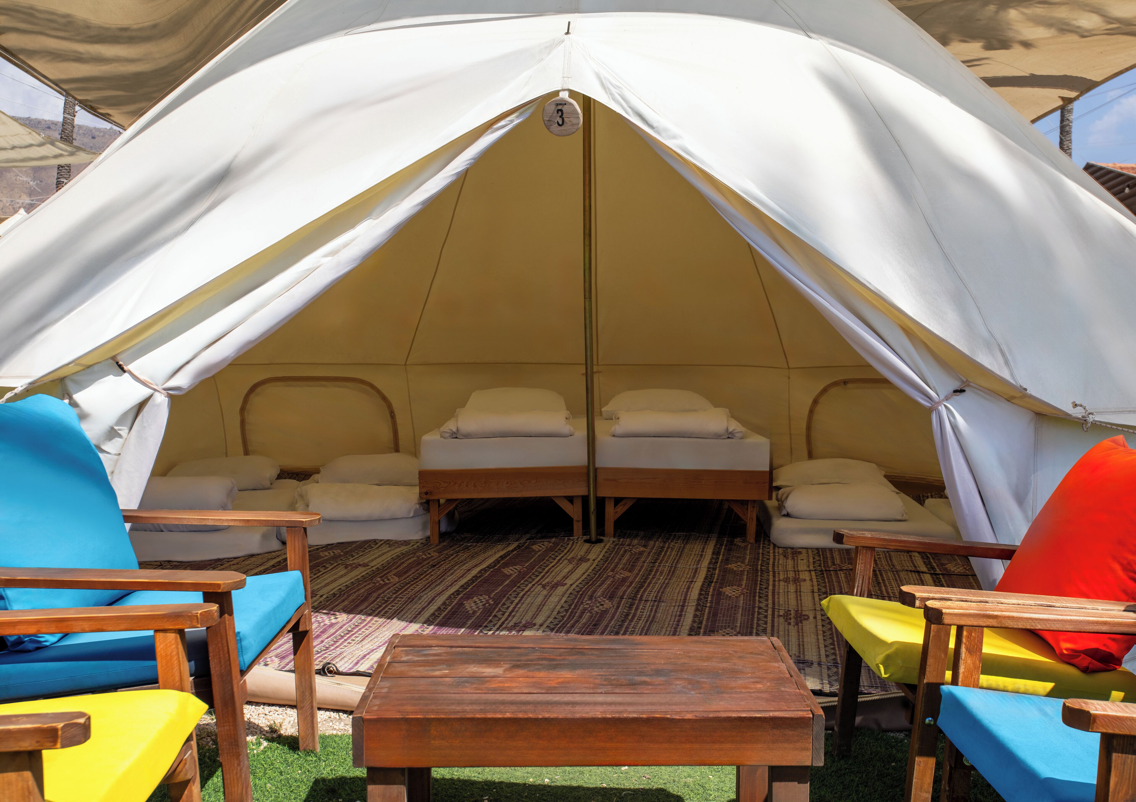 A tent with two beds, a table, and colorful chairs.