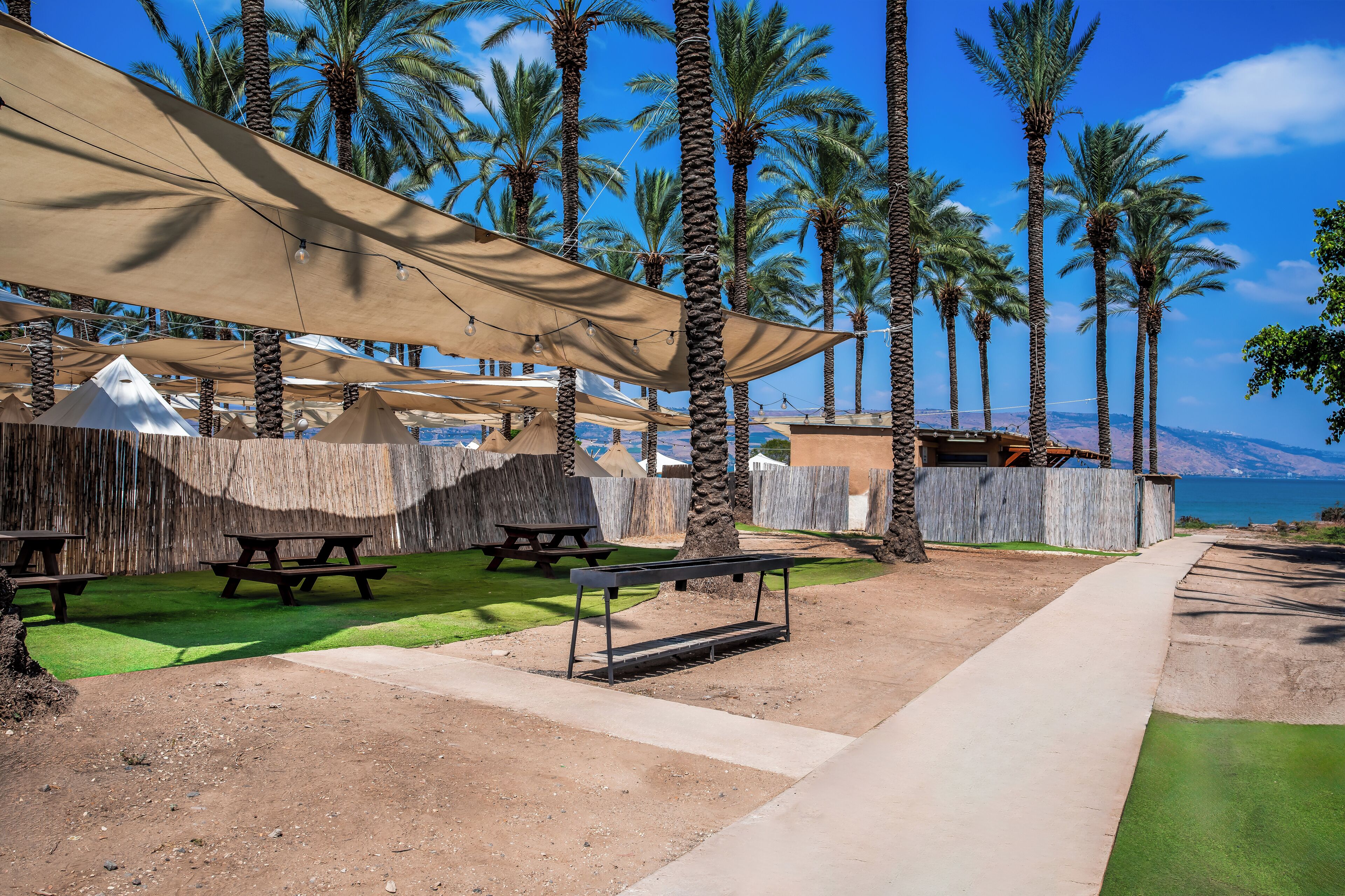 A beachside patio with picnic tables, shade structures, and a view of the sea.