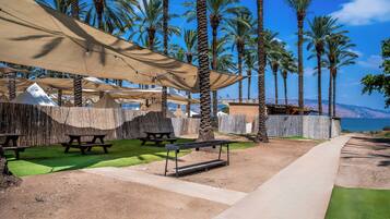 Une terrasse au bord de la plage, dotée de tables de pique-nique, d’abris pour se protéger du soleil et offrant une vue sur la mer.