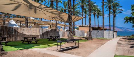 A beachside patio with picnic tables, shade structures, and a view of the sea.
