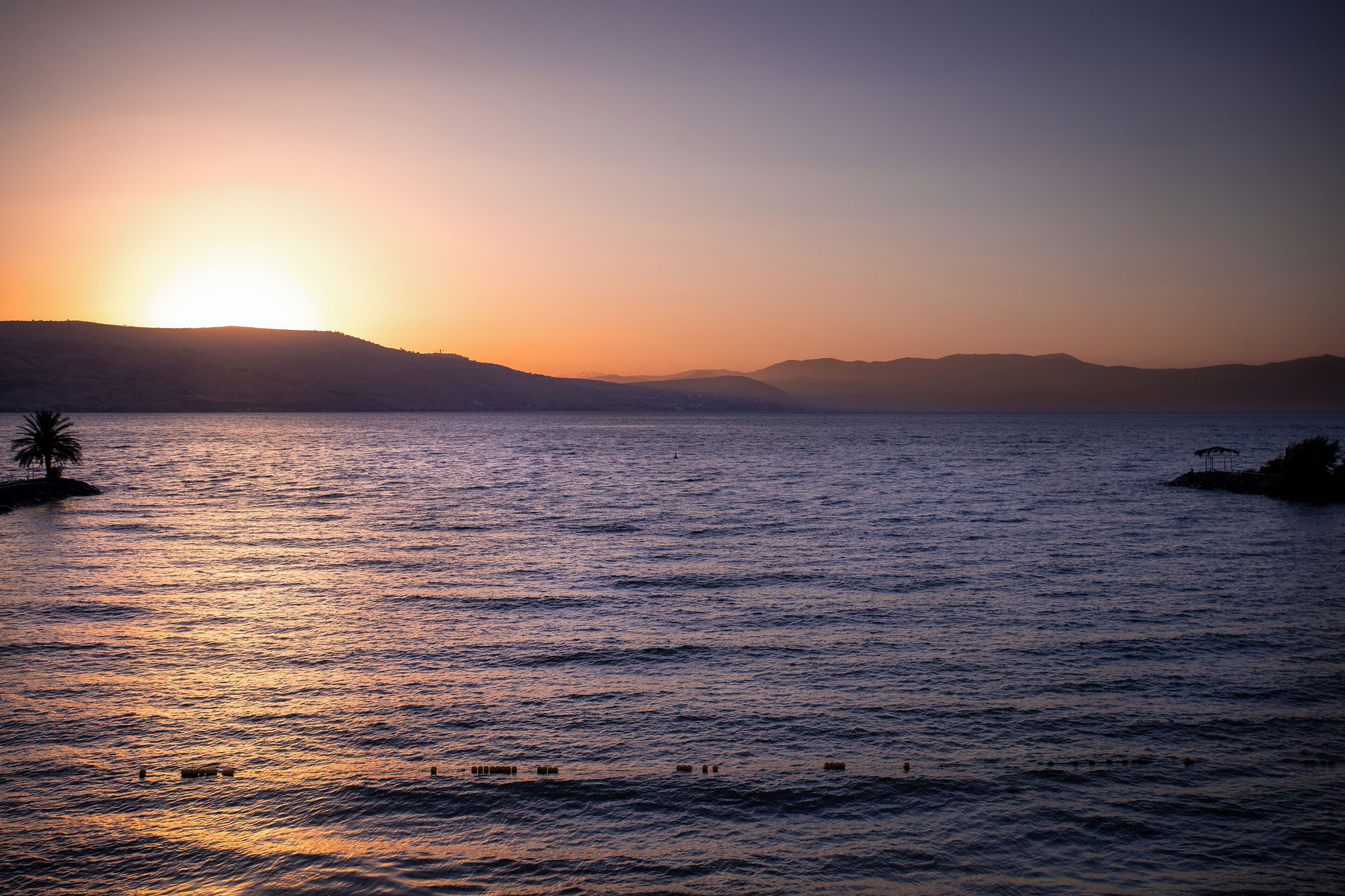 Un coucher de soleil sur une étendue d’eau calme, avec des collines qui se dessinent à l’horizon.