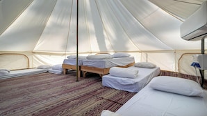 Een tent met meerdere bedden, een centrale paal en een kamerbreed tapijt met een patroon.