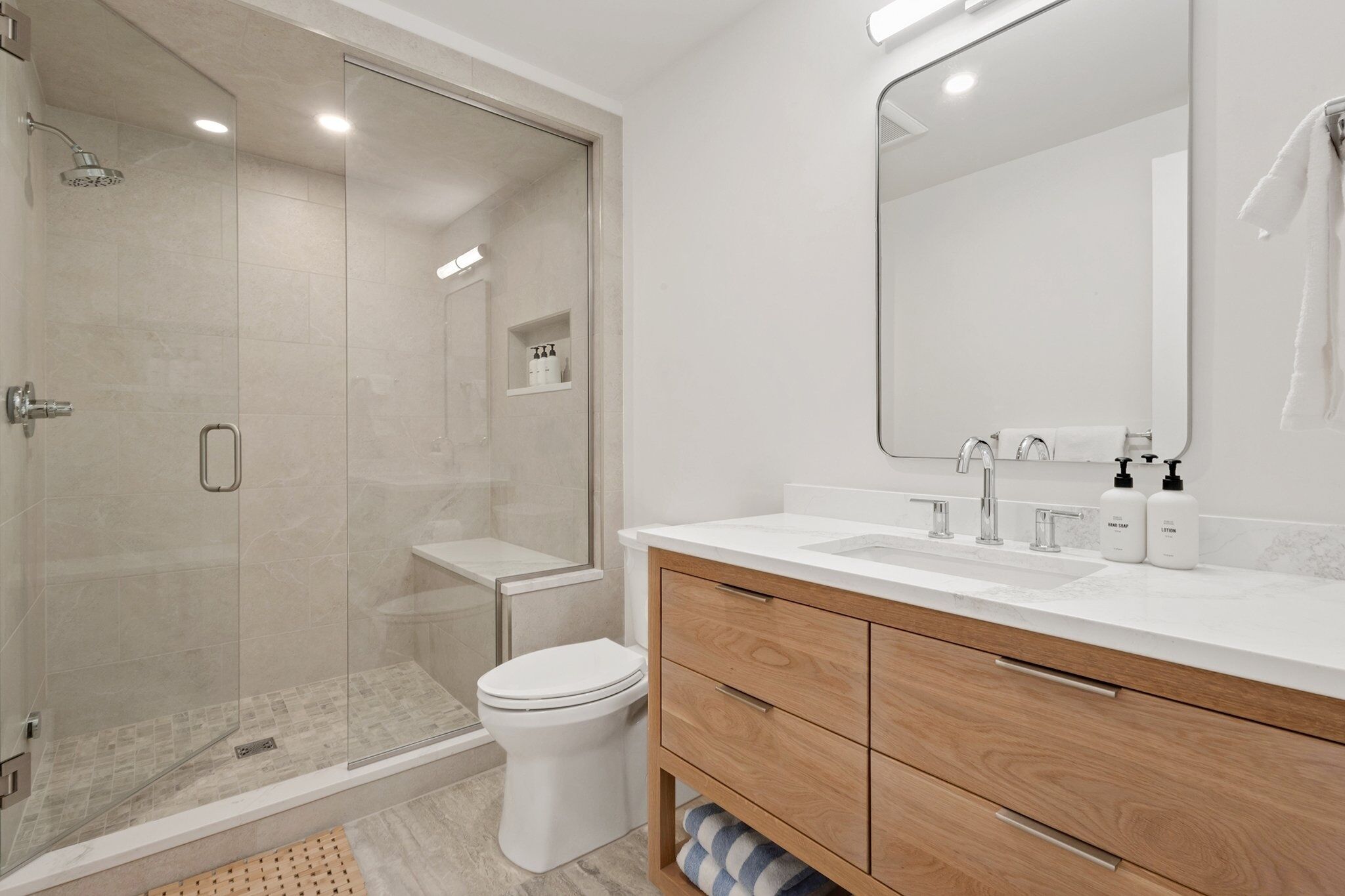 A modern bathroom with a glass-enclosed shower, a toilet, a vanity with a mirror, and a sink.