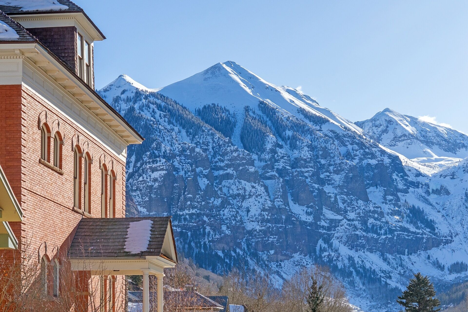 Un bâtiment à la façade en briques et au toit en pente, situé à proximité de montagnes enneigées.
