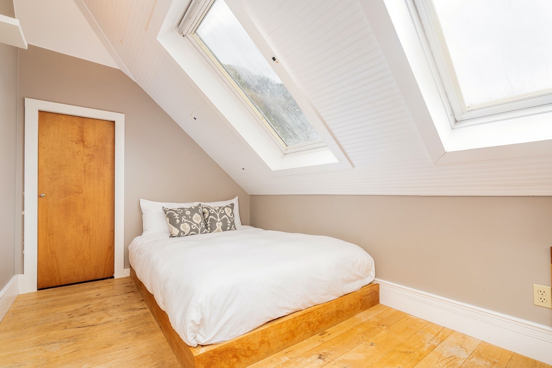 A bedroom with a sloped ceiling, skylights, a wooden bed frame, and a wooden floor.
