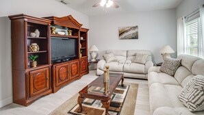 A living room with a wooden entertainment center, a sofa, and a ceiling fan. - Lanai, Private Pool: Lehigh Acres Home (Lehigh Acres)