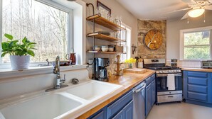 A modern kitchen with a large sink, wooden shelves, a stove, and blue cabinets. - Peaceful Hendersonville Cabin - Hot Tub & Fire Pit (Hendersonville)