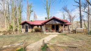 A rustic stone building with a red roof, a wooden porch, and a gravel path leading to the entrance. - Peaceful Hendersonville Cabin - Hot Tub & Fire Pit (Hendersonville)
