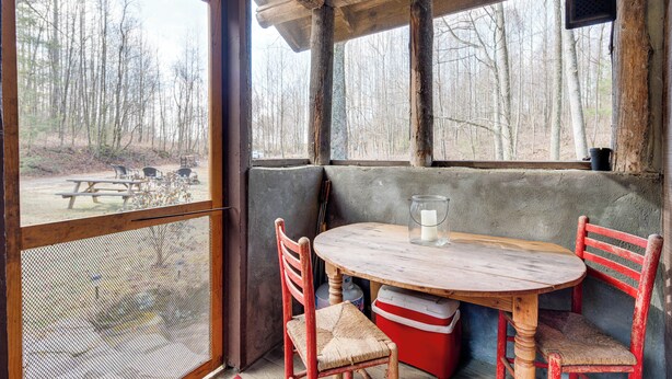 A rustic wooden table with four chairs, a glass of water, and a red cooler. - Peaceful Hendersonville Cabin - Hot Tub & Fire Pit (Hendersonville)