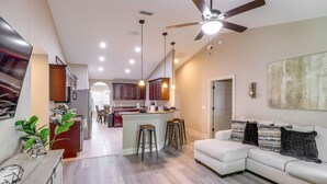 A modern kitchen with wooden cabinets, a central island with stools, a ceiling fan, recessed lighting, and a large painting on the wall. - Ocala Retreat: 4 Mi to World Equestrian Center! (Ocala)