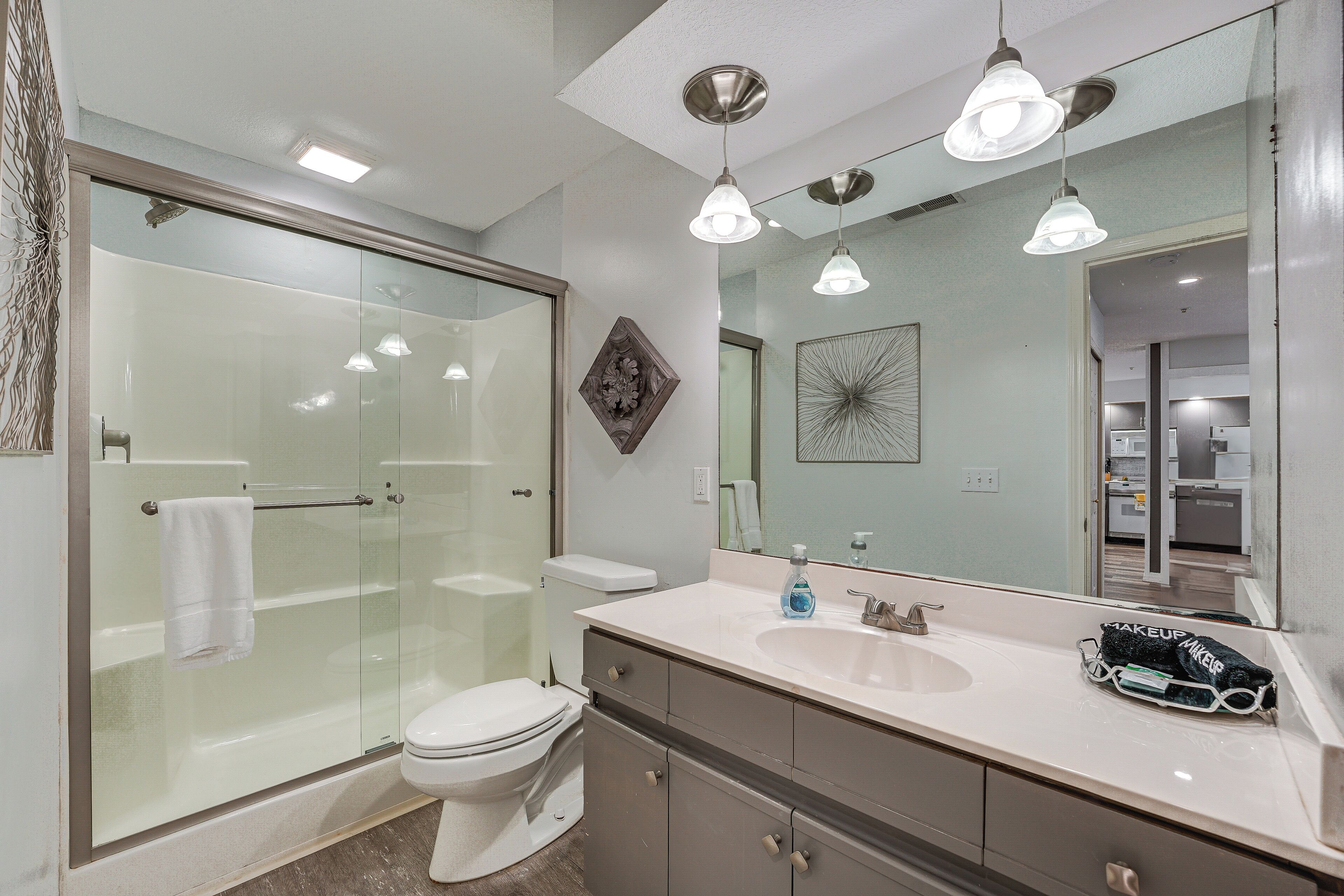 A modern bathroom with a glass-enclosed shower, a white toilet, a vanity with a sink, and a large mirror.