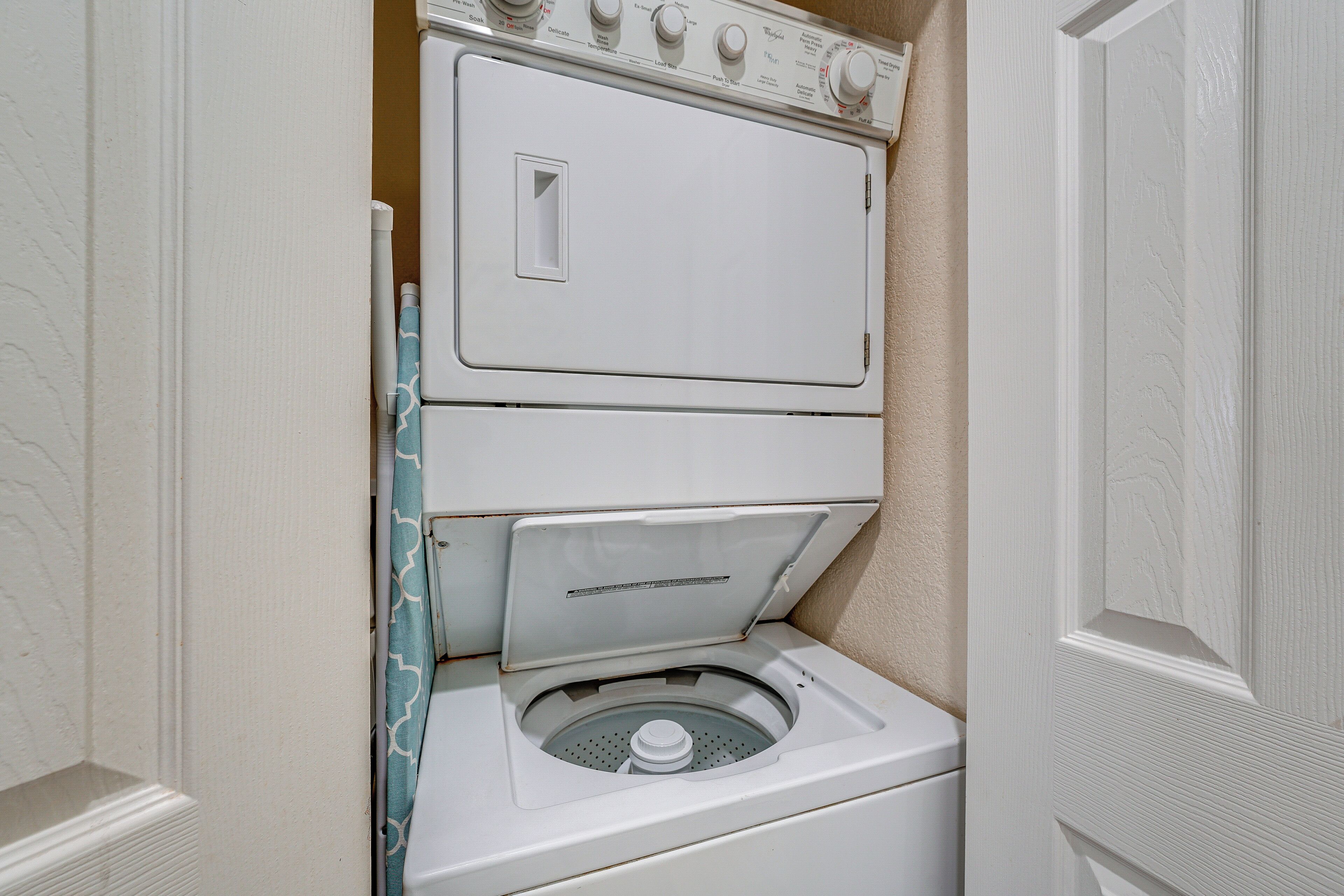 A compact washer and dryer unit in a small laundry room with a door on one side.