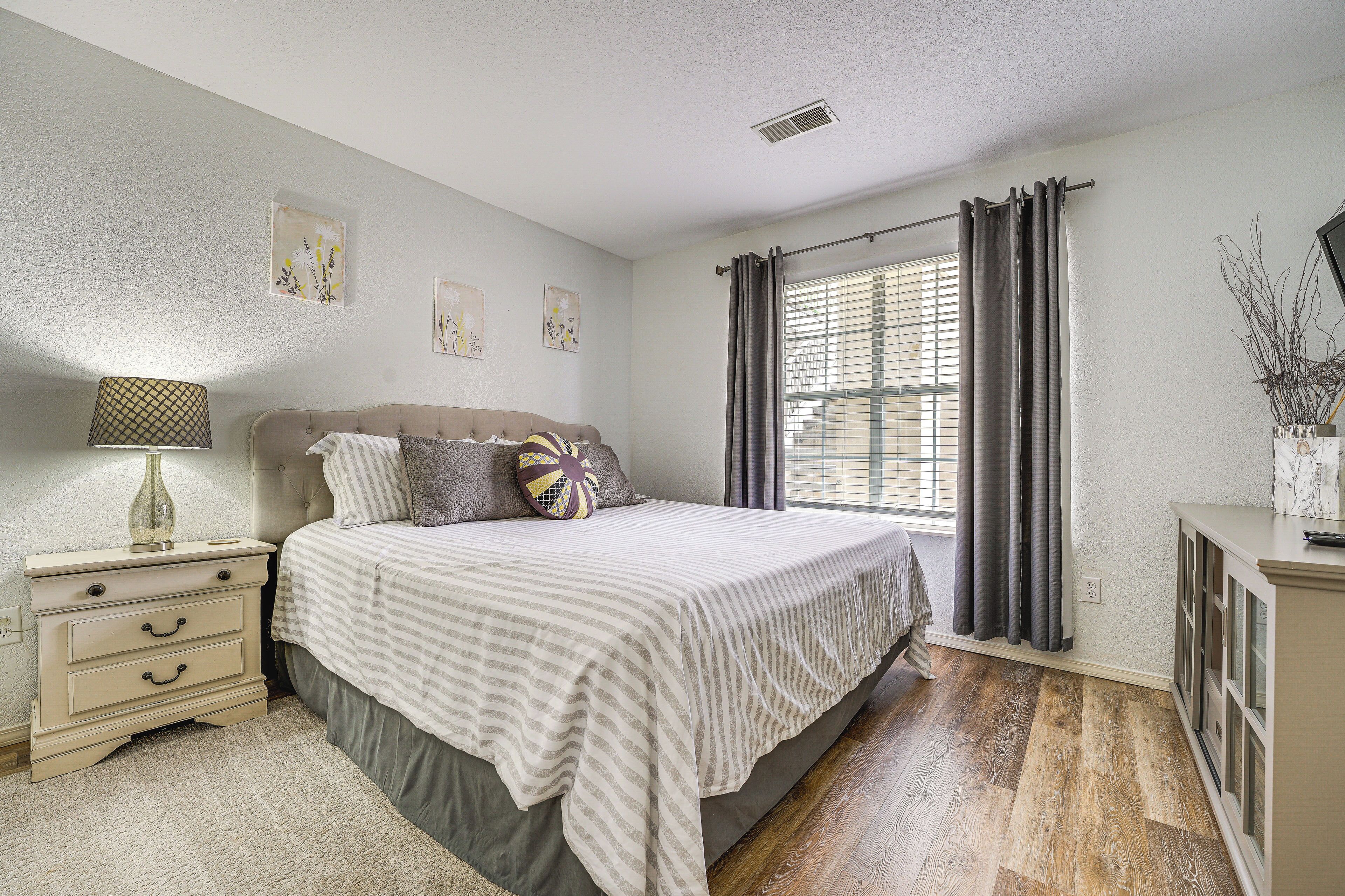A bedroom with a bed, nightstand, dresser, and a window with curtains.