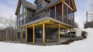 A multi-story house with a balcony, large windows, and a covered outdoor area. - Mountain-view Home in Stoneham w/ Hot Yoga Studio! (Lovell)