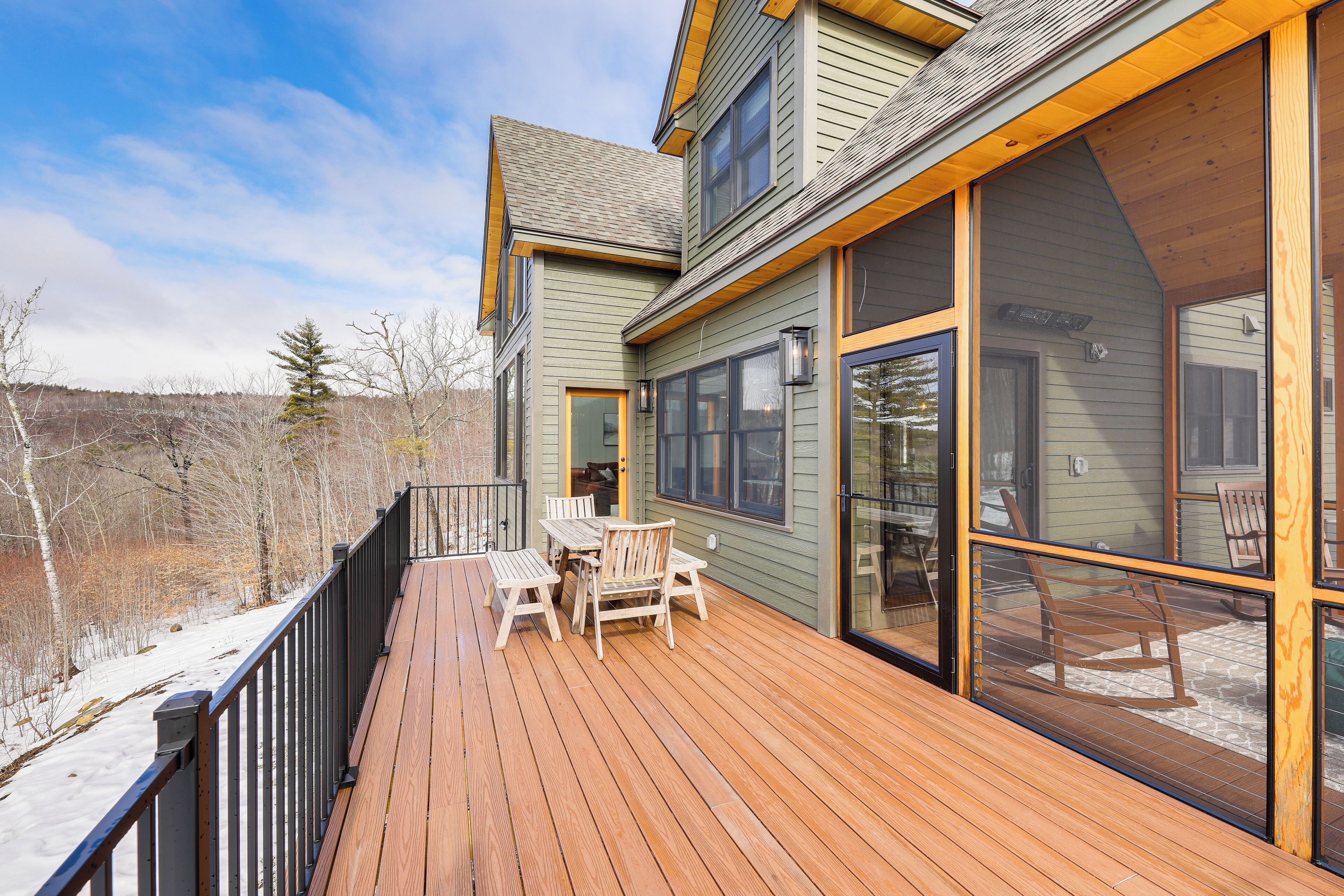 A wooden deck with outdoor furniture, large windows, and a view of a snowy landscape.
