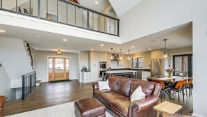 A spacious living area with a leather sofa, ottoman, and dining table with chairs. A staircase leads to an upper level. - Mountain-view Home in Stoneham w/ Hot Yoga Studio! (Lovell)