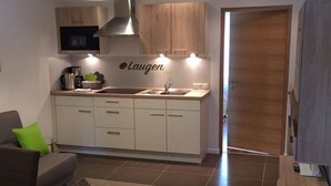 A modern kitchen with white cabinets, a stainless steel sink, and a microwave. There is a logo on the wall above the sink. - Appartment "laugen" (Nals)