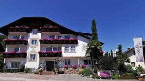 A multi-story building with balconies adorned with flowers, a sign reading "Reinhild," and a well-maintained garden area. - Appartment "laugen" (Nals)