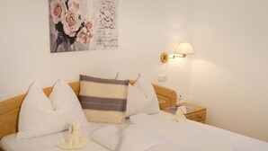 A neatly made bed with white bedding and a striped pillow, a bedside lamp, and a small bedside table with a lamp. - Appartment "laugen" (Nals)