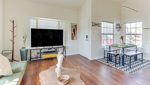 A living room with a large flat-screen TV, wooden flooring, a dining table with chairs, and a sofa. - Game Room, Hot Tub & Grill: Afton Retreat! (Afton)