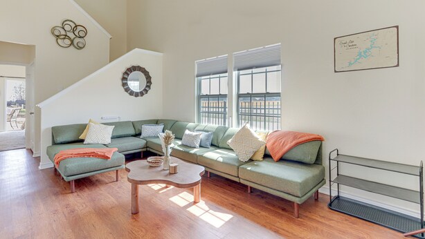 A spacious living room with a green sectional sofa, a wooden coffee table, and a staircase leading to an upper floor. - Game Room, Hot Tub & Grill: Afton Retreat! (Afton)