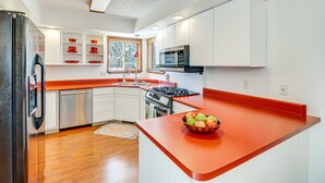 A modern kitchen with white cabinets, a red countertop, stainless steel appliances, and a window providing natural light. - Woodland Park Chalet w/ Deck, Grill & Mtn Views! (Woodland Park)