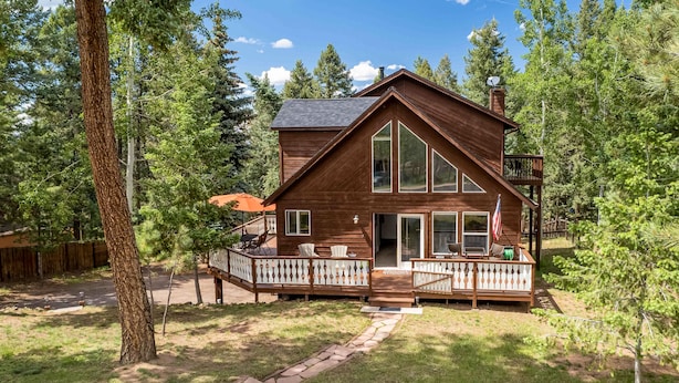 A wooden cabin with a deck, large windows, and an American flag. - Woodland Park Chalet w/ Deck, Grill & Mtn Views! (Woodland Park)