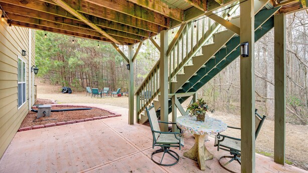 A covered patio with a wooden deck, a table with chairs, and a staircase leading to an upper level. - Pool Table & Patio: Cozy Lawrenceville Apt (Lawrenceville)