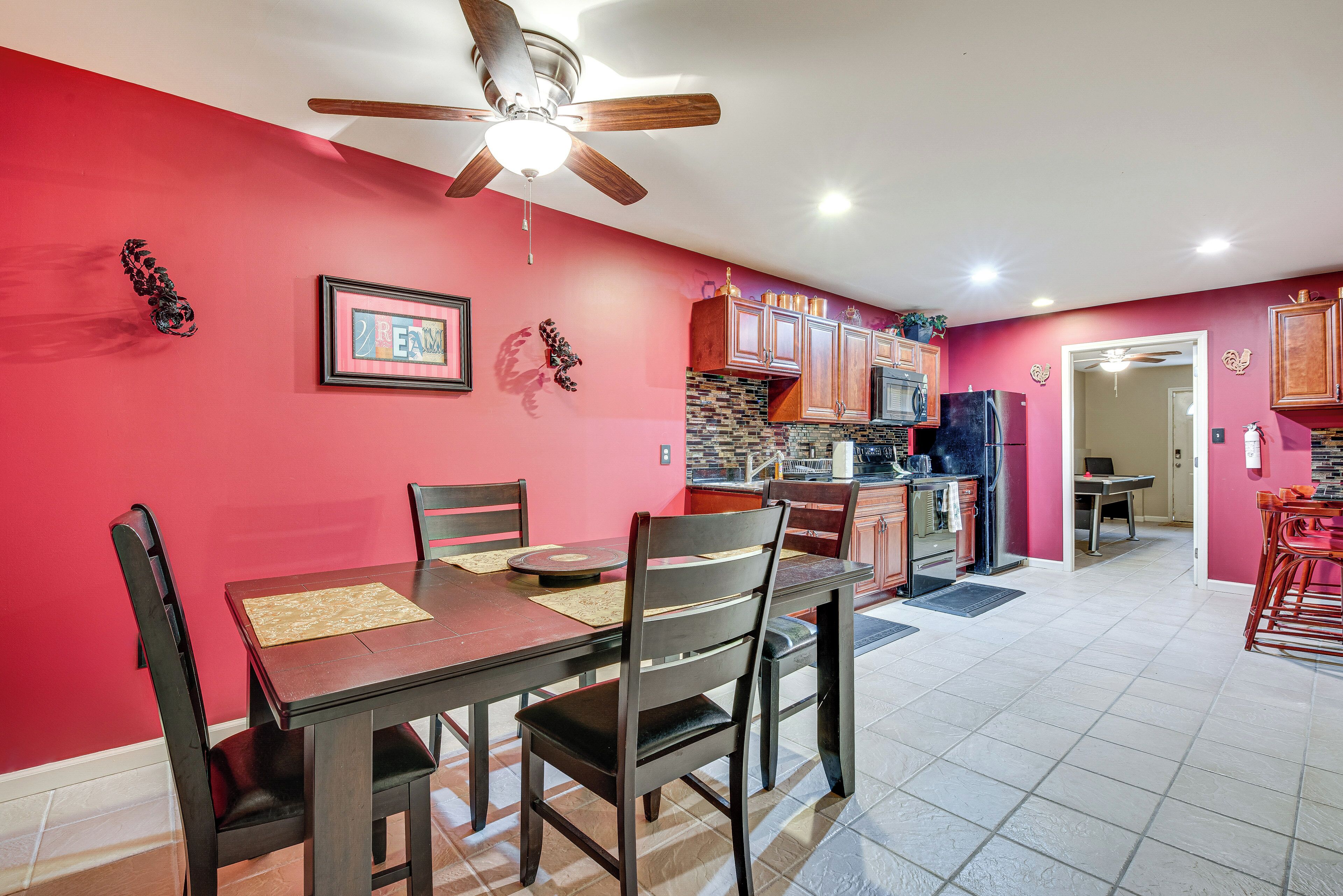 A dining area with a table and chairs, a ceiling fan, and a kitchen in the background.