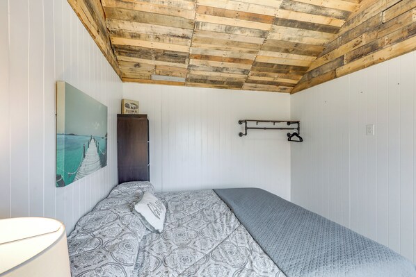 Un dormitorio con techo de madera, una cama con ropa de cama estampada, un estante en la pared y un cuadro de un puente.