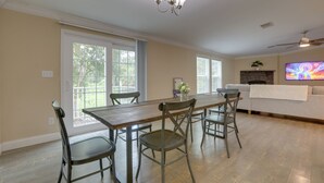 A dining area with a long table, four chairs, a chandelier, and a television in the background.