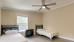 A bedroom with two beds, a window, a ceiling fan, and a dark-colored dresser.