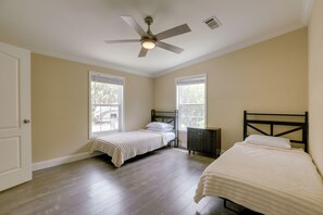 A bedroom with two single beds, a ceiling fan, and large windows.